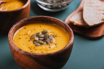 Pumpkin cream soup in bowl on green kitchen table. Autumn delicious food. Closeup