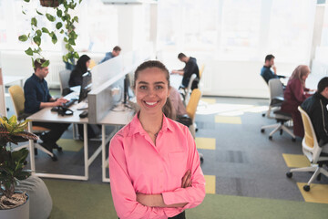 Fototapeta premium Portrait of young smiling business woman in creative open space coworking startup office. Successful businesswoman in modern office. Team of Coworkers working in background.