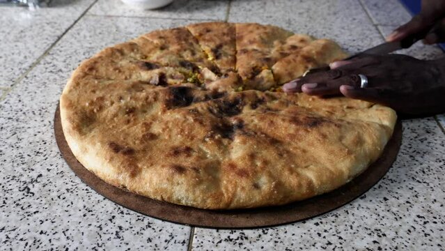 A traditional Moroccan Berber pizza is being cut into pieces. Authentic, a local dish served in Erfoud, Rissani, and Erfoud, South Morocco. Pizza filled with vegetables, meat, eggs, and herbs. 