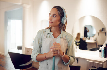 Cleaning, sweeping and salon with a woman cleaner listening to music while working with a broom. Idea, headphones and streaming audio with a female at work in a hairdresser for hygiene or cleanliness