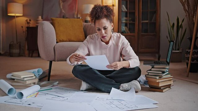 African American woman reads project plan sitting on floor