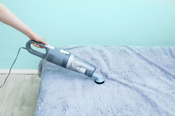 Handheld vacuum cleaner in hand. Vacuuming  fur blanket on the bed.