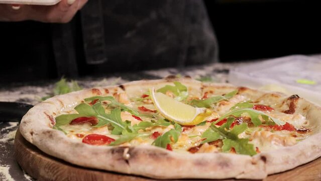 The chef decorates the freshly baked pizza with lamon and sprinkles with cheese. Cream-based pizza with salmon, mozzarella cheese, arugula, tomatoes, parmesan.