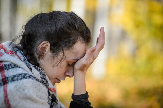 A young woman in an autumn park holds her head with her hand. Headache.