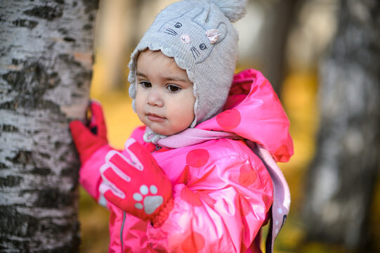 A one-year-old girl in a red jumpsuit on a walk in autumn