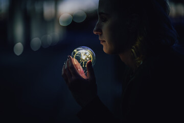 young worried female human holding bright shining lightbulb in her hands feeling unsave while thinking negative about a future blackout with no electricity or power outage with warm background