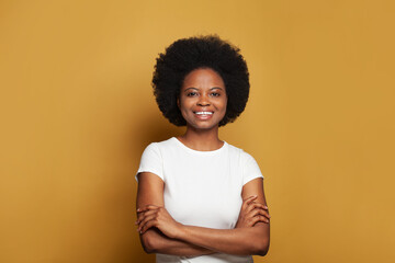 Cute attractive young woman in empty white t-shirt standing with crossed arms and smiling on bright yellow background