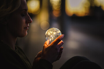 young worried female human holding bright shining lightbulb in her hands feeling unsave while...