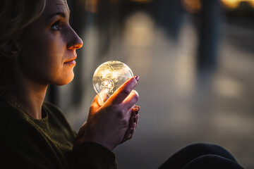 young worried female human holding bright shining lightbulb in her hands feeling unsave while...