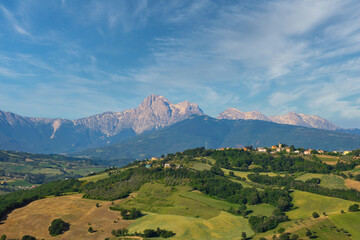 Panoramaansicht auf eine hügelige Landschaft und dem Gebirge Gran Sasso bei leicht bewölkten Himmel in  der Region Abruzzien, Italien - obrazy, fototapety, plakaty