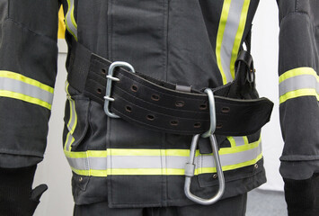 Fototapeta premium Fragment of a black protective fire suit with reflective elements and rescue belt with carabiner