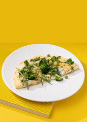 amlet with egg and greens on a white plate on a yellow background