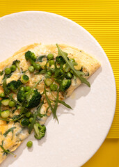 amlet with egg and greens on a white plate on a yellow background