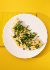 amlet with egg and greens on a white plate on a yellow background