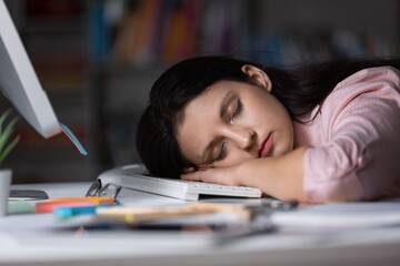 A woman is sleeping, having head on a laptop.