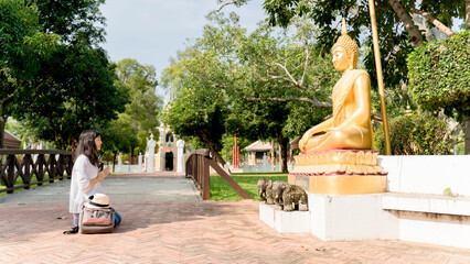 Young Asian woman traveler wearing white shirt and hat praying Buddha statue