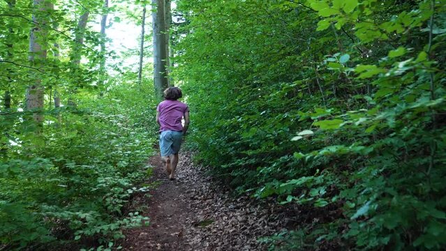 Young man with red tshirt is running up a small path in the forest in slow motion. camera is following him, first person view modus.