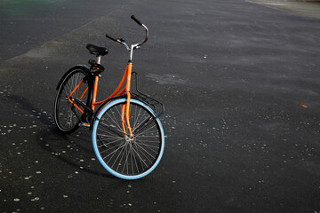Fototapeta na wymiar Orange bike parked on black wet asphalt, mode of transport in Rotterdam