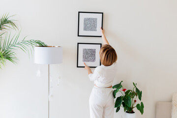 Woman hanging pictures on wall in room. Interior design.