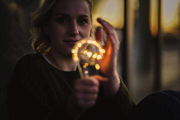 young worried female human holding bright shining lightbulb in her hands feeling unsave while...