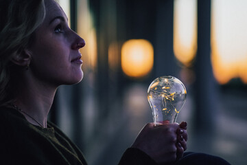 young worried female human holding bright shining lightbulb in her hands feeling unsave while...