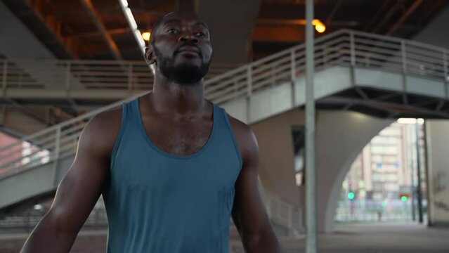 4k Young male athlete works out and jumps in city spbas. African american man doing exercise and stretching his body, getting ready for boxing training on bridge in modern town. Handsome black guy