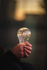 young smiling woman holding bright shining lightbulb in her hands while thinking optimistic about...