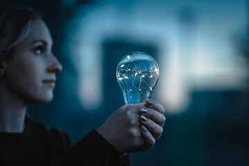 young worried woman holding bright shining lightbulb in her hands feeling unsave while in fear...