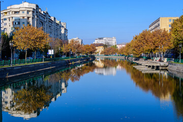 Landscape with Dambovita river, old buildings and yellow, orange and brown leaves in large trees in the center of Bucharest, Romania, in a sunny autumn day.