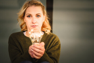 young worried female human holding bright shining lightbulb in her hands feeling unsave while...