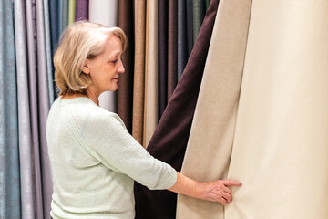 Woman touching fabric in store indoor. Customer choosing textures and colors of curtains in shop