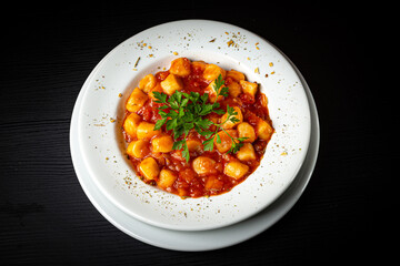 Gnocchi dish with tomato sauce and parsley on rustic wooden table.