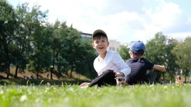 two boys sit on the grass in the park and feed the pigeons