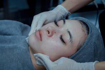 Obraz na płótnie Canvas Beautician cleaning hydrogel mask on young woman's face after using cold cryotherapy in beauty salon, beauty clinic concept