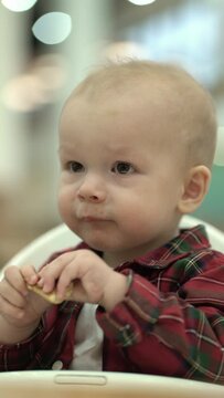 Little boy eats baby cookies while sitting in a baby chair.