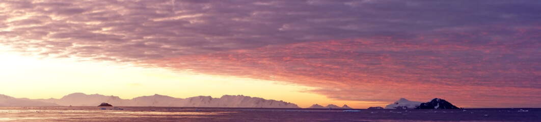 Panorama of a colorful sunset over mountains and a field of floating icebergs at Cierva Cove, Antarctica