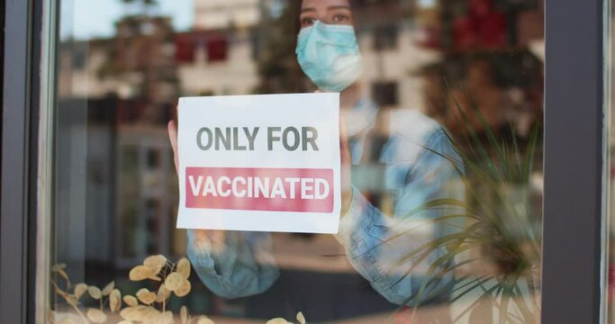 Only for vaccinated. Descrimination. Vax. Vaccination. Covid-19. Close up of womans hands attaching sign on the glass in pandemic time. Pandemic of coronavirus.