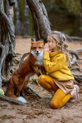 Little beautiful girl with a fox in the autumn forest. Friendship of a girl and a fox. Love of wild...