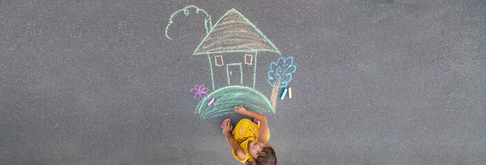 The child draws a house on the asphalt. Selective focus.