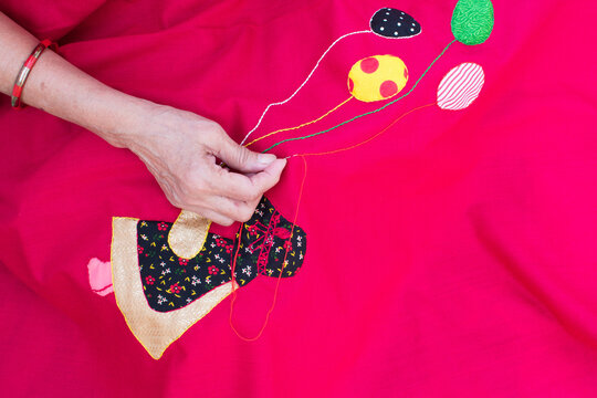 Closeup of a woman's hands sewing applique work making doll and balloon with chain stich in baby’s quilt or bed sheet. Concept of self employment woman and Female entrepreneurs in India.