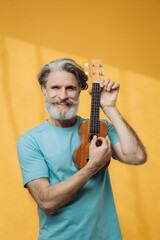 Studio portrait of senior retired elderly man playing ukulele.