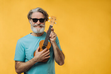 Studio portrait of an elderly man in sunglasses playing a ukulele.