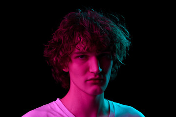 Looks offended. Closeup portrait of young man, student in white tee isolated on dark background in neon light. Concept of emotions, facial expression, youth