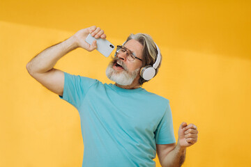 Optimistic gray-haired old man listens to music, dances, wears headphones, glasses, isolated on...