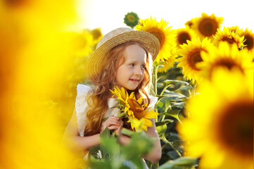 Girl wearing straw hat with a sunflower in hands looking to the side