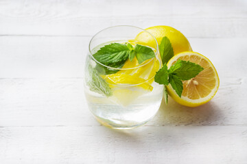 Homemade lemonade with lemon, mint and ice cubes in a glass on the white wood table with lemons.