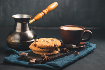 Crispy oatmeal cookies with raisins, coffee cup and turkish coffee pot, chocolate chunks on a dark background