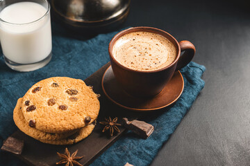 Crispy oatmeal cookies with raisins, coffee cup, milk glass, and chocolate chunks on a dark background