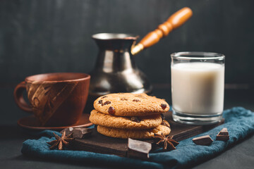 Crispy oatmeal cookies with raisins, glass with milk and turkish coffee pot on a dark background