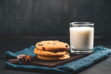 Crispy oatmeal cookies with raisins and glass with milk on wooden board, dark background